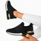 Zapatillas casual negras y doradas de diseño moderno, calzadas por una modelo con jeans blancos, perfectas para estilos urbanos y deportivos.