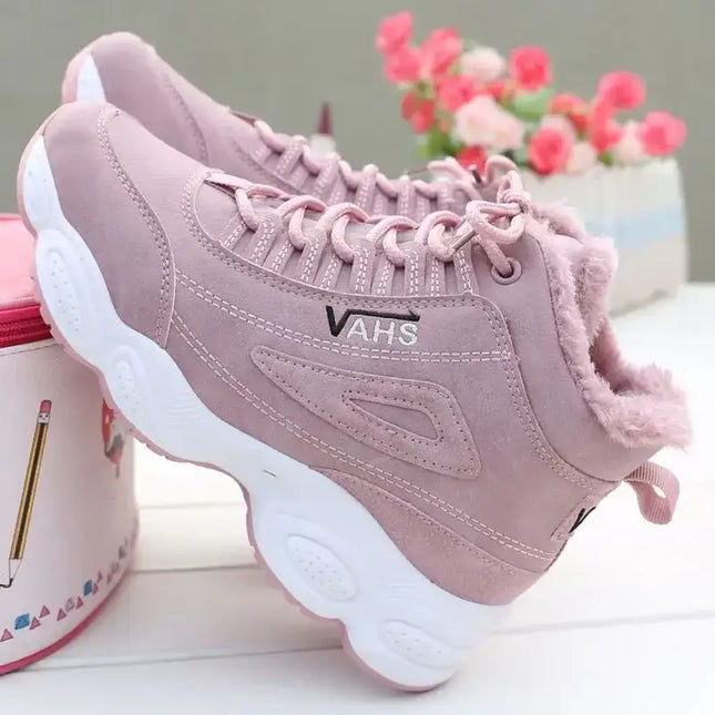 Zapatillas deportivas rosas con forro cálido, ideales para invierno, sobre una mesa con flores en el fondo. Botas de mujer.