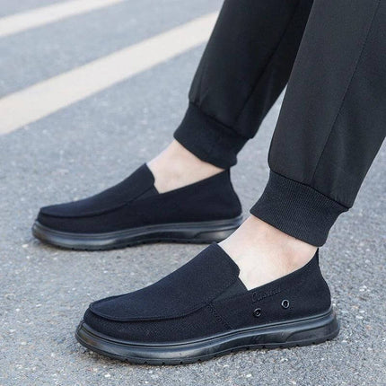 Zapatos de lona negra casuales para hombre, ideales para caminar, sobre una vereda gris.