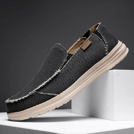 Zapato informal transpirable de lona negra para hombre, diseño moderno sobre fondo gris, suela beige